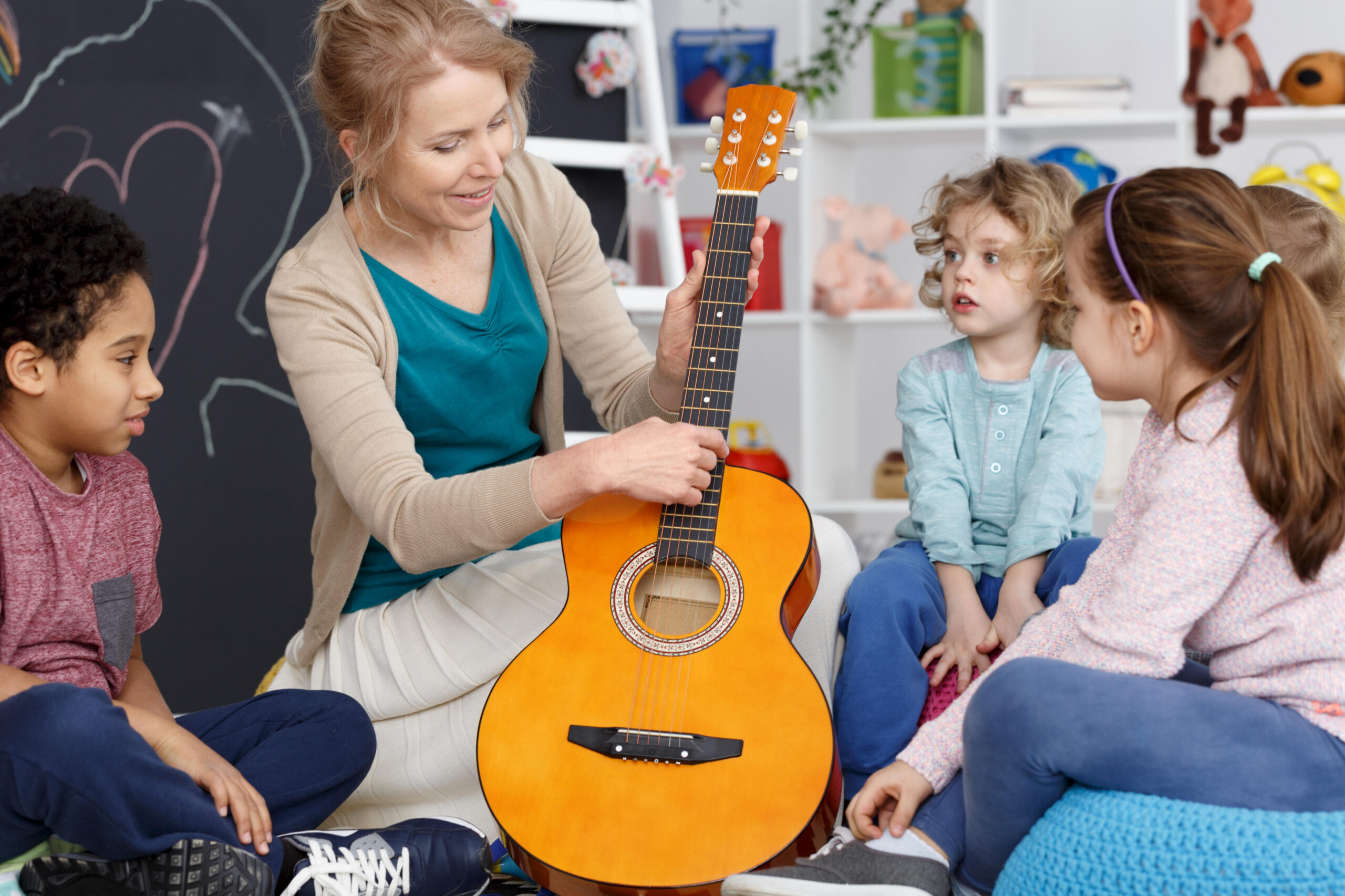 Kindergarten teacher showing kids how to play the guitar